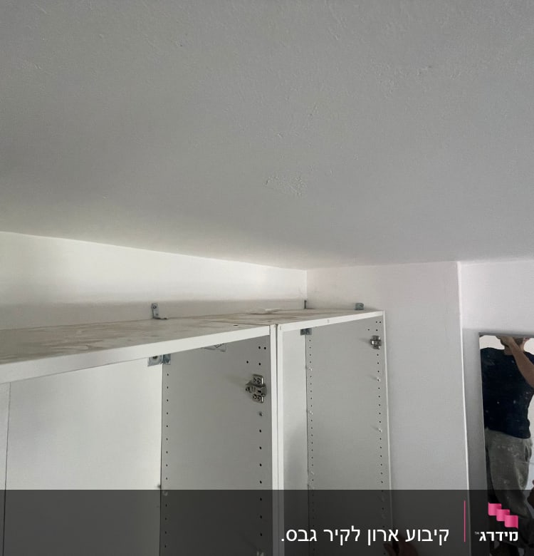 אדם מתקין ארון קיר לבן עם מדף עליון